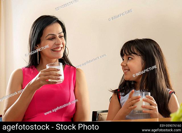 A HAPPY DAUGHTER AND MOTHER LOOKING AT EACH OTHER WHILE DRINKING MILK