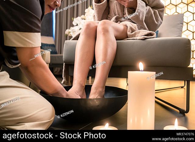 Young woman drinking organic tea during traditional Chinese foot massage in luxury spa and beauty center
