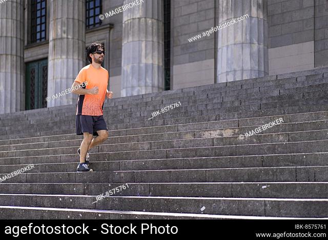 Portrait of handsome attractive mature bearded athletic latin man guy 40s in orange t-shirt running on some stairs