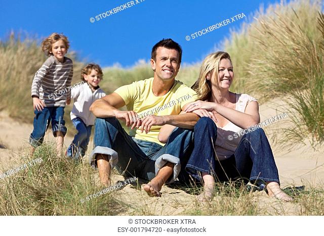 A happy family of mother, father and two sons, sitting and having fun in the sand dunes of a sunny beach