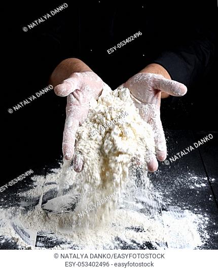 white wheat flour in male hands, black background