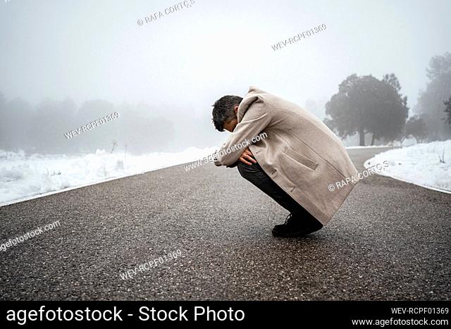 Lonely man hugging knees on road