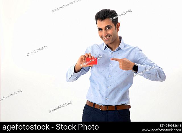 A CONFIDENT CORPORATE MAN LOOKING AT CAMERA AND POINTING TOWARDS BUSINESS CARD IN HAND