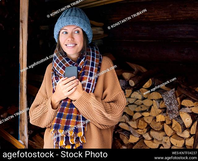 Young woman near a woodpile holding smartphone
