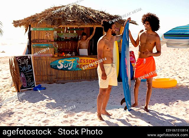 Mixed race men holding surf board on beach