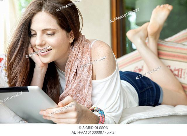 Young woman lying on stomach, looking at digital tablet