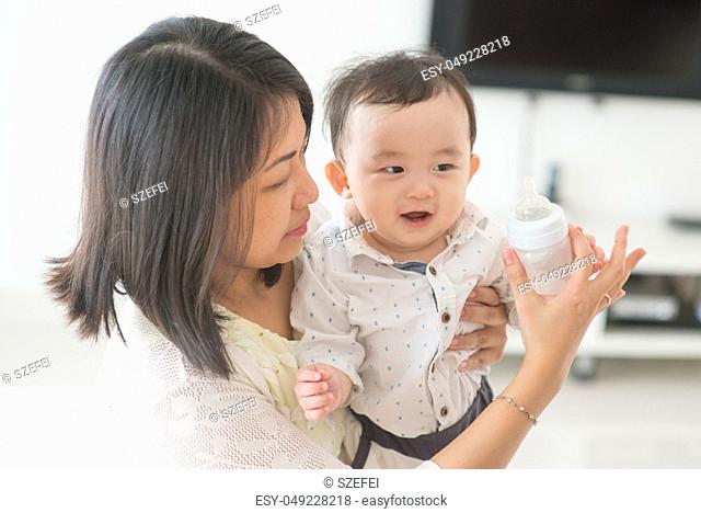Mother holding milk bottle with 9 months old child. Asian family at home, living lifestyle indoors