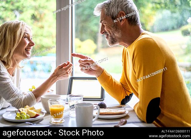 Smiling mature couple talking with each other while having breakfast