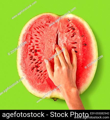 Simulation of masturbation, female fingers touch inside fresh ripe watermelon fruit on a lawn green background with copy space. Easy eroticism