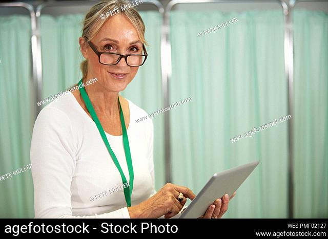 Smiling female doctor with eyeglasses holding tablet PC in medical room