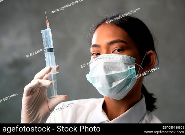 Closeup of young female doctor with syringe. Woman physician in protective mask portrait over concrete wall background