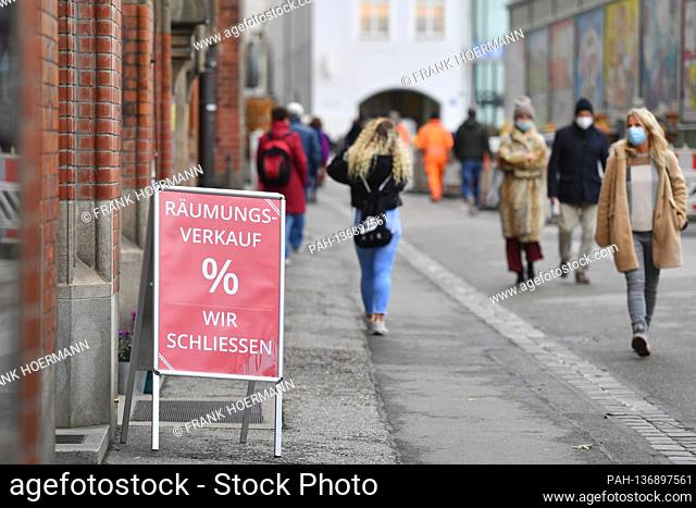 Subject picture CLEARANCE SALE, WE CLOSE. Passers-by walk with face masks, masks in the pedestrian zone in Munich past a display that indicates closure