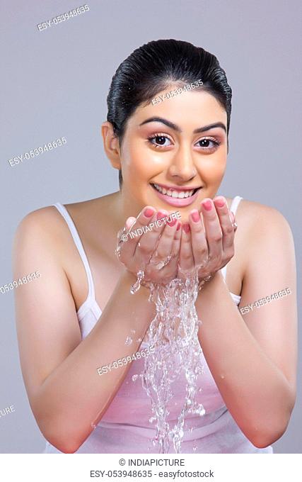 Portrait of young woman washing face with water over gray background