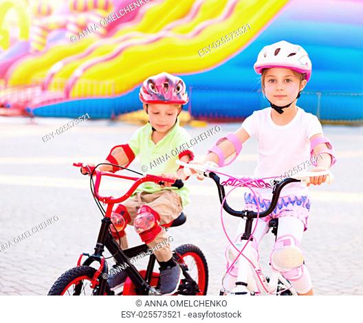 Happy friends on the bicycles, brother with sister having fun in amusement park, playing game outdoors, enjoying friendship and summer holidays
