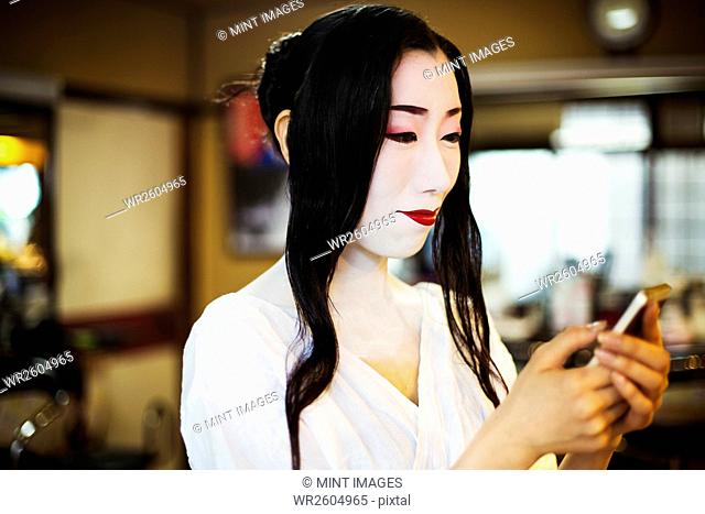 Geisha with long black hair and traditional white face make up using a smart phone