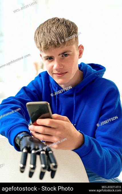 Boy with prosthetic arm using smart phone sitting on chair