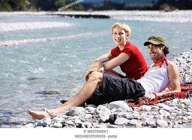 Germany, Bavaria, Tölzer Land, Young couple sitting on riverbank