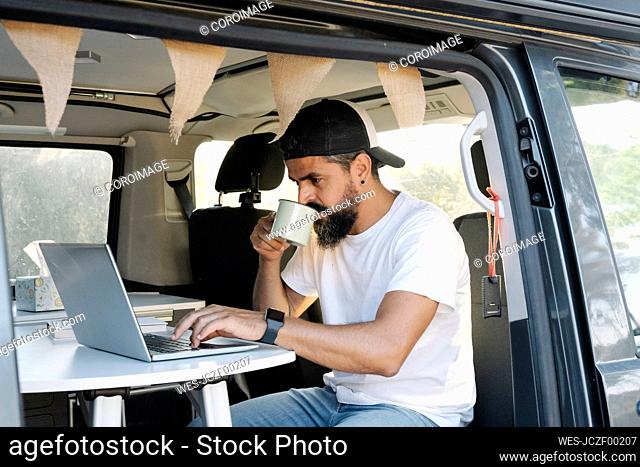 Mature man using laptop while sipping coffee in van