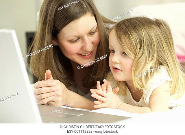 Mother and daughter lying in bed while using laptop