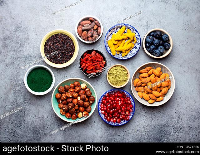 Set of different superfoods in bowls on stone gray background: spirulina, goji berry, cocoa, matcha green tea powder, quinoa, chia seeds, blueberries