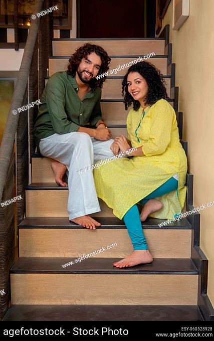 Young couple posing in front of camera while sitting on stairs at home