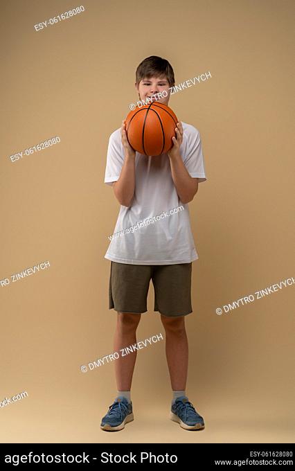 Full-length portrait of an adolescent with the basketball in his hands posing for the camera against the beige background