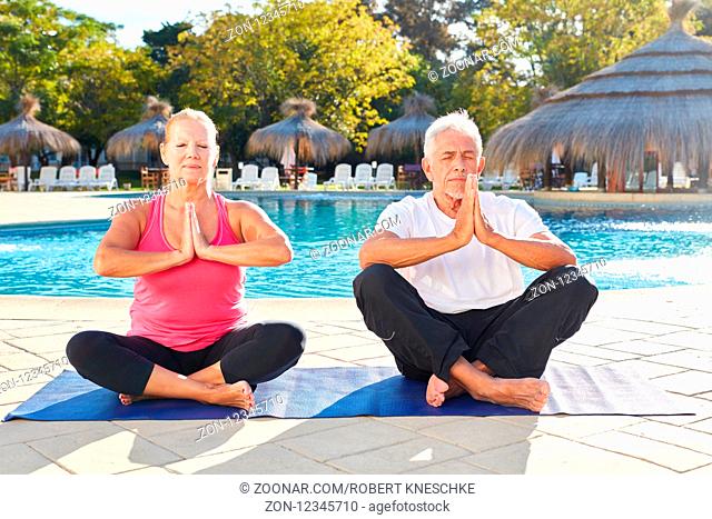 Senioren Paar sitzt am Pool und macht eine Meditation mit gefalteten Händen
