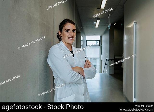 Smiling scientist standing with arms crossed at clinic corridor