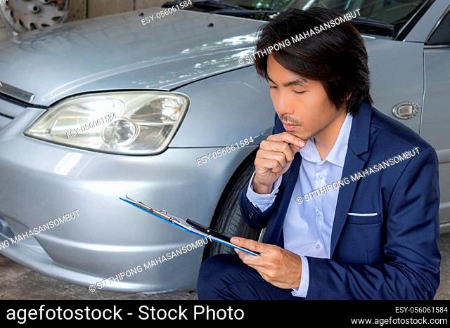 Asian Insurance Agent or Insurance Agency in Suit Reading Data Report and See Smartphone of Car Crash from Accident for Claim at Outdoor Place