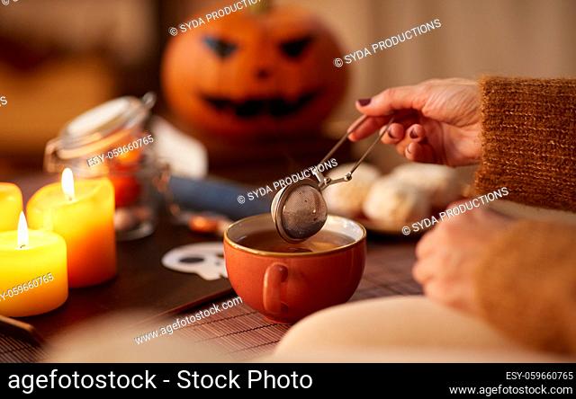 woman's hand with tea infuser and mug on halloween