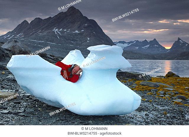 tourist lying on stranded iceberg, Ikasaulaq Fjord, Greenland, Ammassalik, East Greenland, Kuummiit