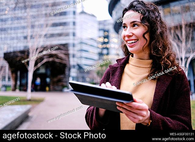 Smiling female professional holding digital tablet while looking away