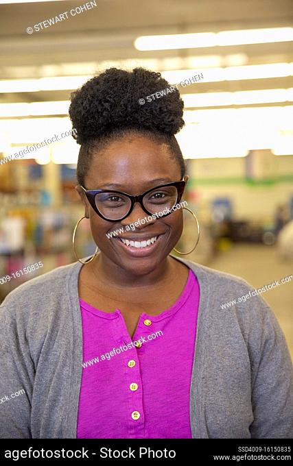 Portrait of smiling woman wearing retro glasses and large hoop ear rings, looking at camera smiling