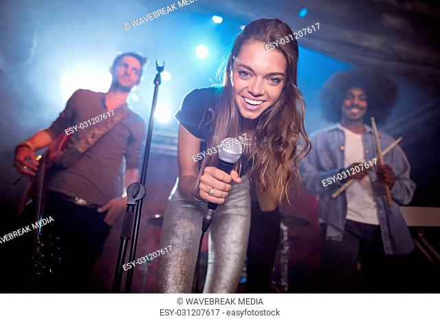 Cheerful young singer with musicians performing at nightclub