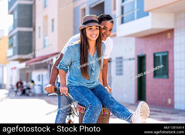 Interracial couple have fun together riding a bike in outdoor in the city - happiness and joy young people interracial boyfriend and girlfriend - two enjoy...