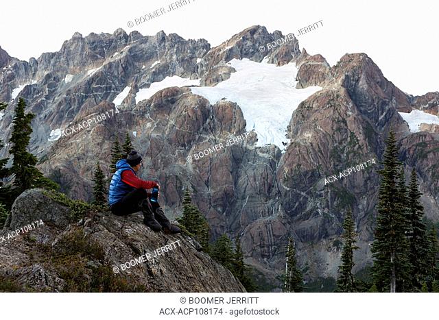 A lone hiker looks up to the Septimus/Rousseau massif and it's hanging glacier while camping overnight on the Flower Ridge trail, Strathcona Park
