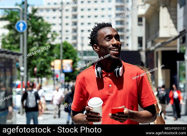 Smiling man holding mobile phone and coffee cup
