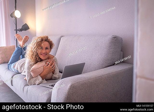 beautiful young woman working by lying in front of laptop on sofa. portrait of happy businesswoman working from home. woman spending leisure time using laptop...