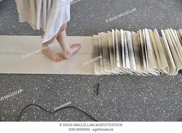 A side view from the knees down of a woman artist in a white dress turning as she creates a performance art work at an artist run gallery in Windsor, Canada