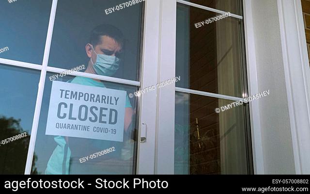 Small business owner turns the sign on her storefront from open to closed because of coronavirus pandemic. Sign in a shop window: TEMPORARILY CLOSED