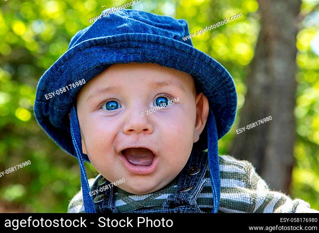 Portrait of cute little infant with blue eyes hat sitting in park with mouth wide open enjoying and relaxing outdoor garden