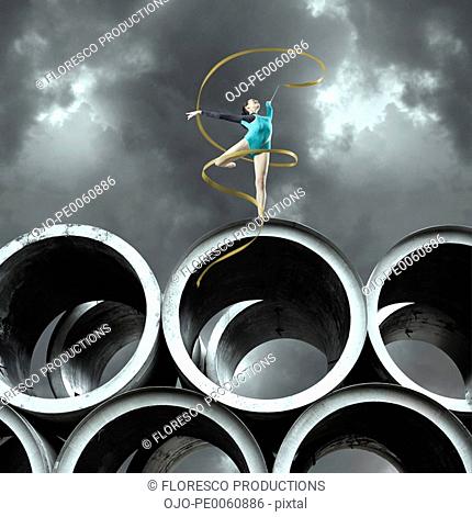 Woman gymnast outdoors on large cement cylinders posing with ribbon
