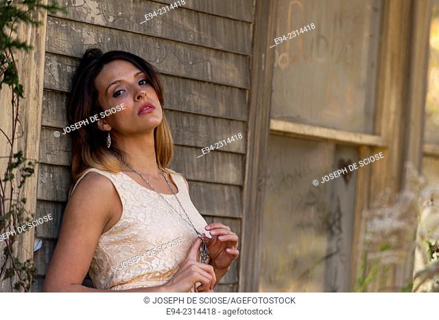 30 year old brunette woman looking at the camera wearing a dress standing in front of an old house in the country