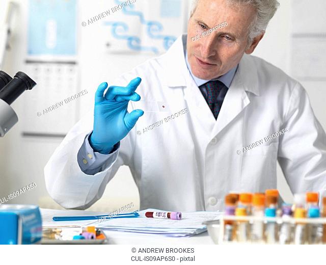 Doctor viewing patients blood slide under microscope with other samples for testing
