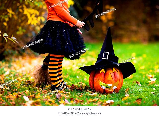 Little girl in witch costume playing in autumn park. Child having fun at Halloween trick or treat. Kids trick or treating
