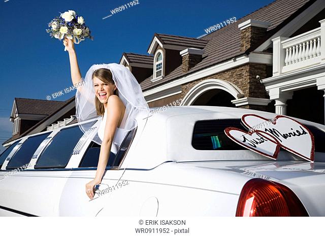 A bride holding a bouquet of flowers and leaning out of a limo window