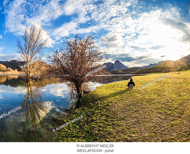 Spain, Asturias, Camposolillo, Cantabrian Mountains, senior man sitting at seashore of Porma reservoir enjoying the sunshine