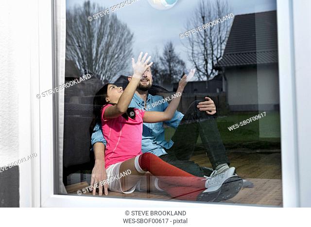 Girl in soccer outfit sitting next to father on floor in living room playing with soccer ball