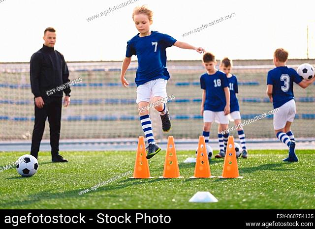 Kids on sports soccer training. Boys running balls and jumping over cones. Agility exercises for youths in football team