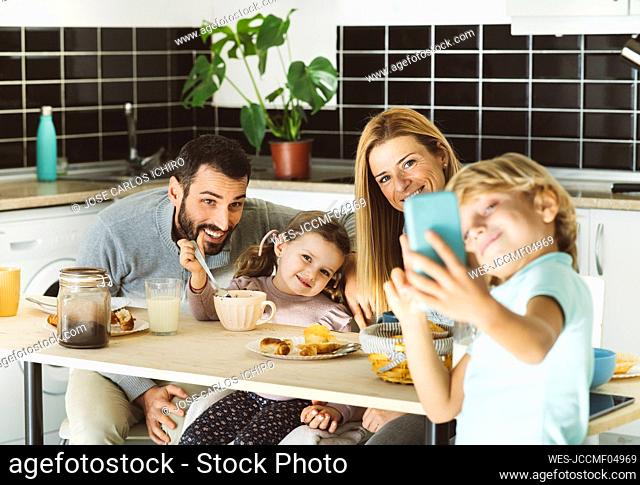 Boy taking selfie with happy family at breakfast table